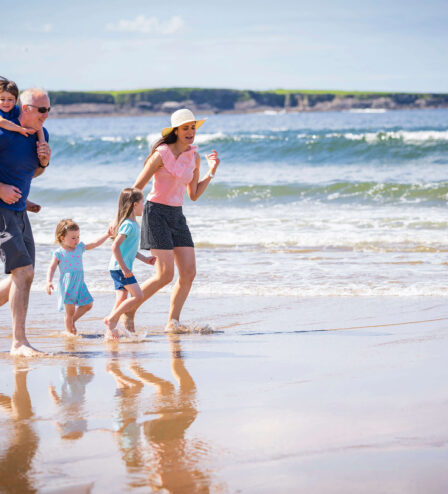 A family joyfully strolling along a sunny beach with gentle ocean waves.