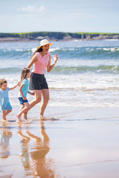 A family joyfully strolling along a sunny beach with gentle ocean waves.