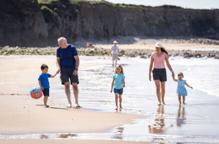 Family enjoying a sunny day walking along the sandy beach with cliffs in the background.