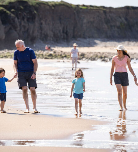 Family enjoying a sunny day walking along the sandy beach with cliffs in the background.