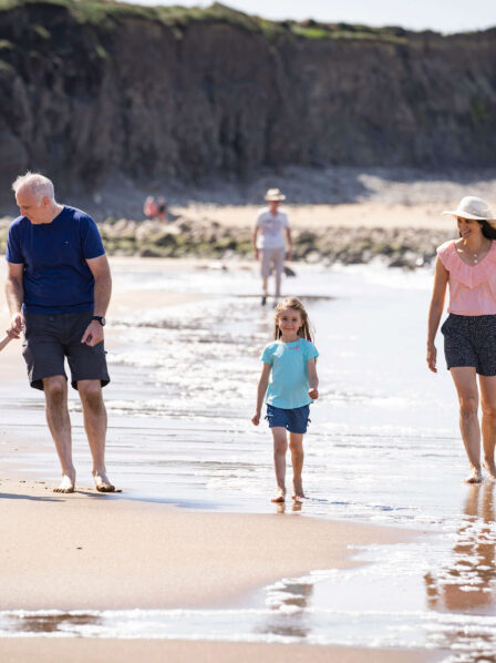 Family enjoying a sunny day walking along the sandy beach with cliffs in the background.