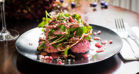 Fresh, vibrant salad with pecans and beetroot puree on a black plate in a cosy hotel restaurant.