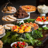 Elegant dessert display with cakes, scones, and tarts on a wooden table in a cosy hotel setting.