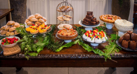 A variety of delicious desserts on a wooden table with fresh fruits and greenery.