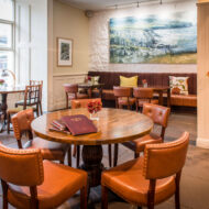 Warm hotel dining room with cosy seating, art, and soft lighting.