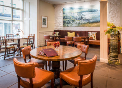 Warm hotel dining room with cosy seating, art, and soft lighting.