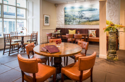 Warm hotel dining room with cosy seating, art, and soft lighting.