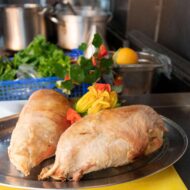Freshly roasted meat on a platter with vibrant vegetables in a hotel kitchen setting.