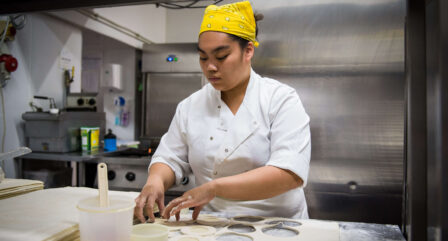 Chef in a hotel kitchen preparing dough with round cutters and a focused expression.