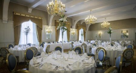 Elegant dining room with round tables set for an event, featuring chandeliers and floral centrepieces.