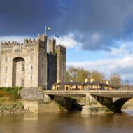 Majestic castle by the river with a charming bridge under a partly cloudy sky.