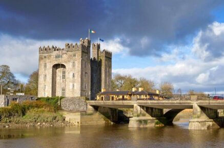 Majestic castle by the river with a charming bridge under a partly cloudy sky.