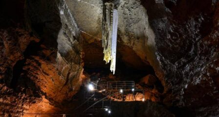 Family exploring an illuminated cave with dramatic stalactites and textured rock walls.