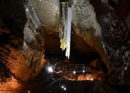 Family exploring an illuminated cave with dramatic stalactites and textured rock walls.