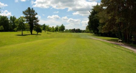 Lush green hotel grounds under a bright sky with scattered clouds, surrounded by trees.