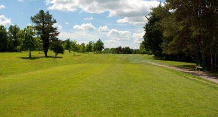 Lush green golf course under a blue sky, surrounded by trees, at a peaceful hotel setting.