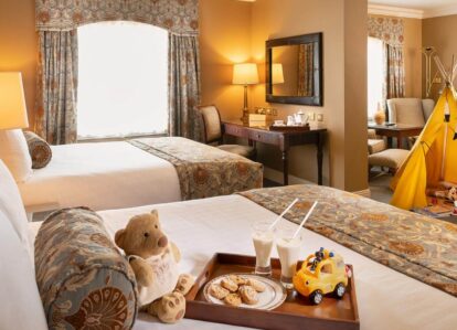 Cosy hotel room with two beds, a children's play tent, and a welcoming tray of biscuits and milk.