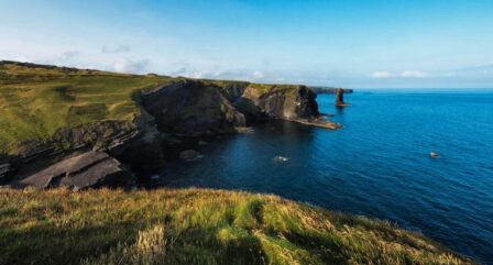 Scenic coastal cliffs with lush greenery and calm blue sea under a clear sky.