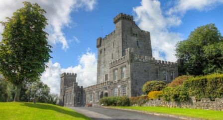 A historic stone castle hotel amidst lush greenery under a bright blue sky.