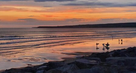 Serene beach sunset with surfers enjoying the waves, reflecting warm orange hues.