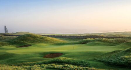 A serene golf course at sunrise, surrounded by rolling green hills near a distant stone ruin.
