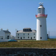 A family enjoys a sunny day near a historic lighthouse and seaside hotel.