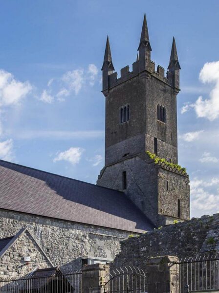 Historic stone church with tall spires under a blue sky, surrounded by lush greenery.