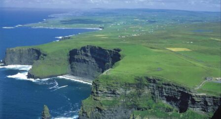 Scenic view of the Cliffs of Moher and lush green fields meeting the Atlantic Ocean on a sunny day.