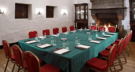Cosy meeting room with a large table, red chairs, notepads, and a warm fireplace at Old Ground Hotel.