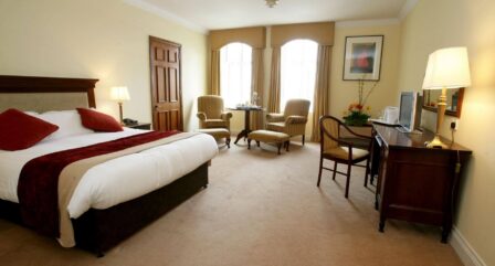Spacious hotel room with a comfortable double bed, chairs by the window, and a cosy desk area.