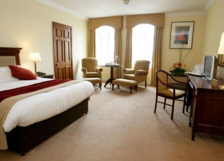 Spacious hotel room with a comfortable double bed, chairs by the window, and a cosy desk area.