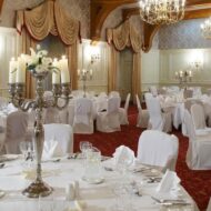 Elegant hotel ballroom set for a formal event with round tables, white linens, and chandeliers.
