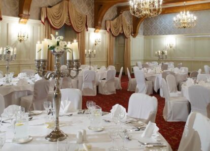 Elegant hotel ballroom set for a formal event with round tables, white linens, and chandeliers.