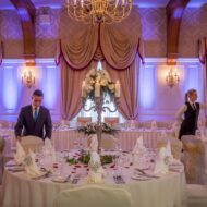 Elegant dining hall set for an event with staff preparing tables in warm, inviting ambiance.