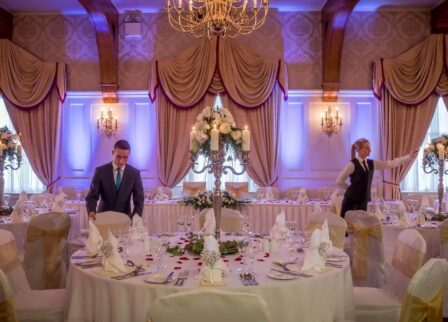 Elegant dining hall set for an event with staff preparing tables in warm, inviting ambiance.