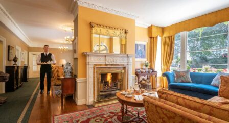 Elegant hotel lounge with fireplace, cosy seating, and waiter serving afternoon tea.