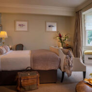 Cosy hotel room with plush bed, elegant decor, window seating, and wine on the table.