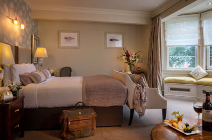 Cosy hotel room with plush bed, elegant decor, window seating, and wine on the table.