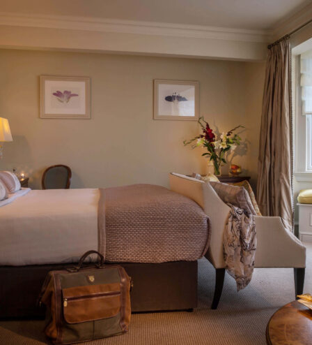 Cosy hotel room with plush bed, elegant decor, window seating, and wine on the table.