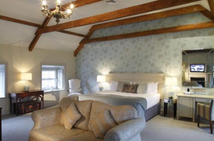Elegant hotel room with cosy sofa, large bed, and wooden beams, creating a warm, inviting atmosphere.