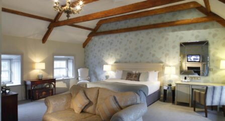 Elegant hotel room with cosy sofa, large bed, and wooden beams, creating a warm, inviting atmosphere.