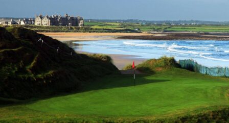 Scenic coastal view of a golf course near Old Ground Hotel, with ocean waves and lush greenery.