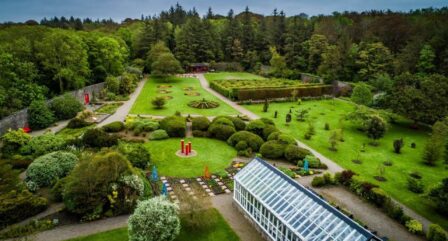 Aerial view of a lush garden with winding paths and a glasshouse, surrounded by trees.