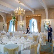 Elegant dining room set for an event, with staff preparing tables under grand chandeliers.