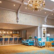 Elegant hotel lounge with blue velvet seating, a chandelier, and a welcoming bar area.