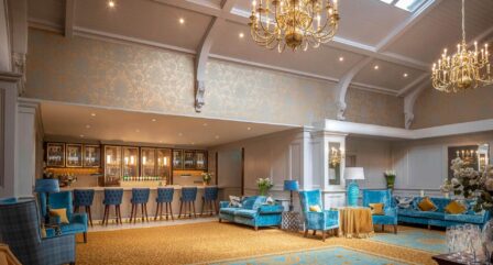 Elegant hotel lounge with blue velvet seating, a chandelier, and a welcoming bar area.