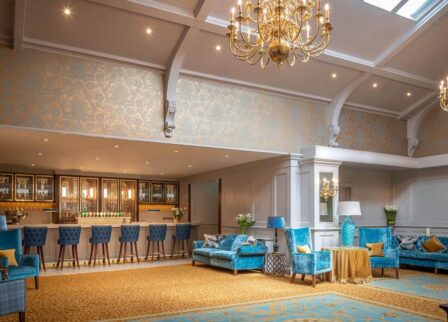 Elegant hotel lounge with blue velvet seating, a chandelier, and a welcoming bar area.