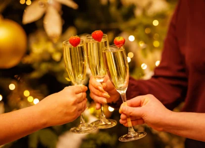 A group toasts with champagne glasses adorned with strawberries near a festive tree.