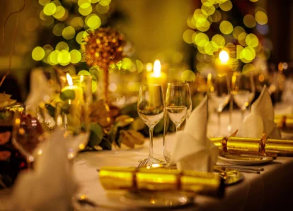 Festive dining table with lit candles, golden decorations, and Christmas crackers.